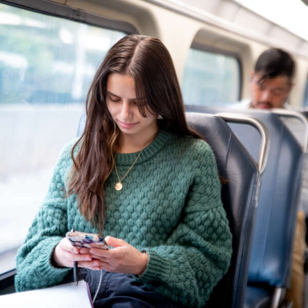 A young woman in a green sweater looks at her smartphone on a Metra train.