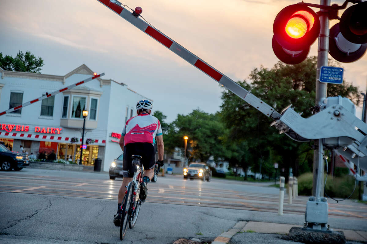 A person on a bike waiting at a railroad crossing at sunset in a suburban neighborhood.
