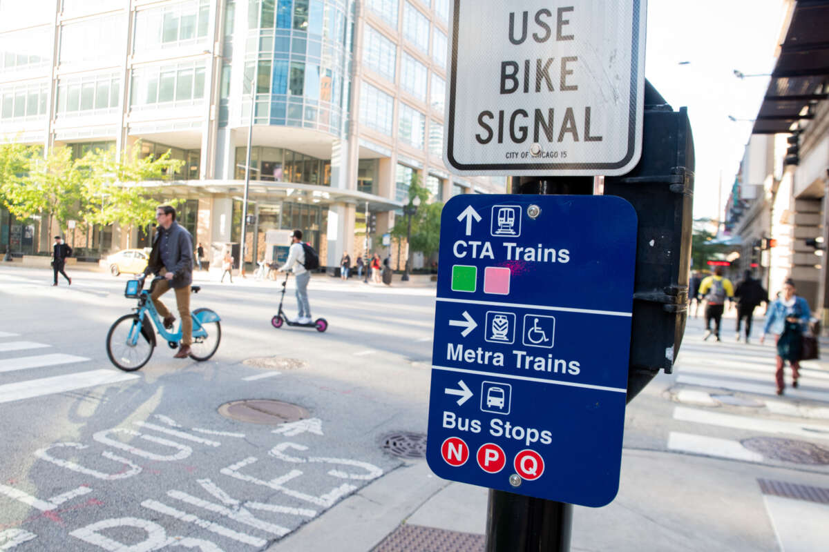 Signage for CTA trains, Metra trains, and Bus stops with person on Divvy bike in background.