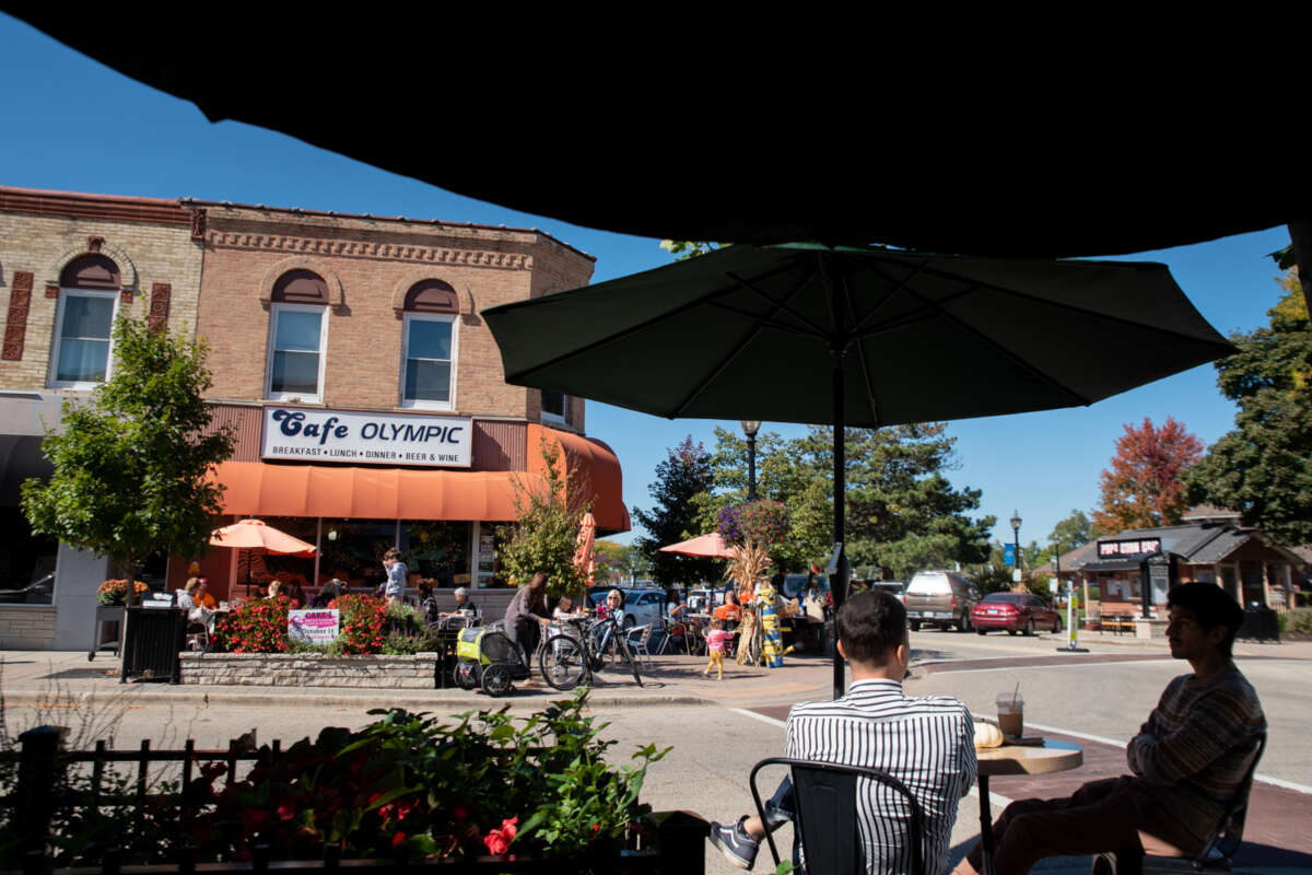 People outdoor dine on patios in Crystal Lake, including someone with a bicycle hauling a trailer.