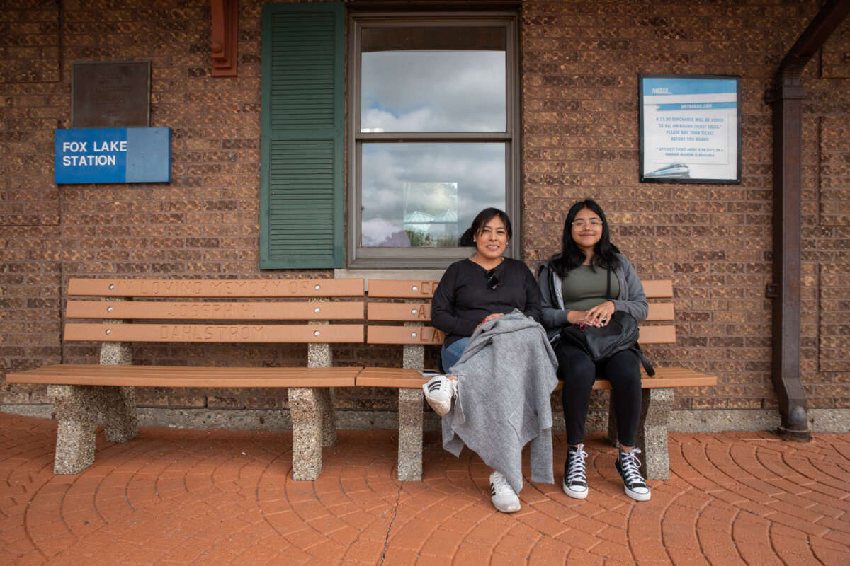 Two women sit on a bench at the Fox Lake Metra station.