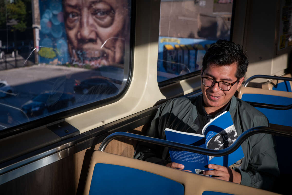 Man reads a book on a CTA Blue Line train with a mural visible out the train window.