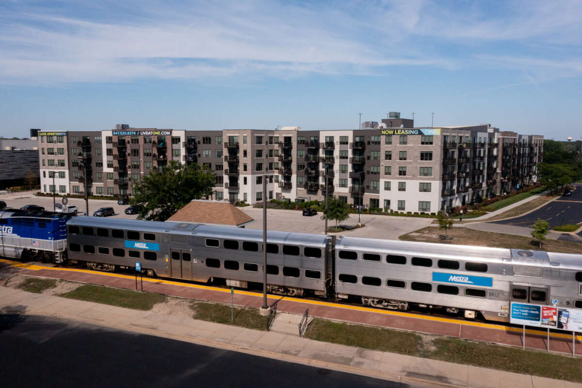 Large, dense new housing development with "now leasing" signs behind a Metra train at the Wheeling station.