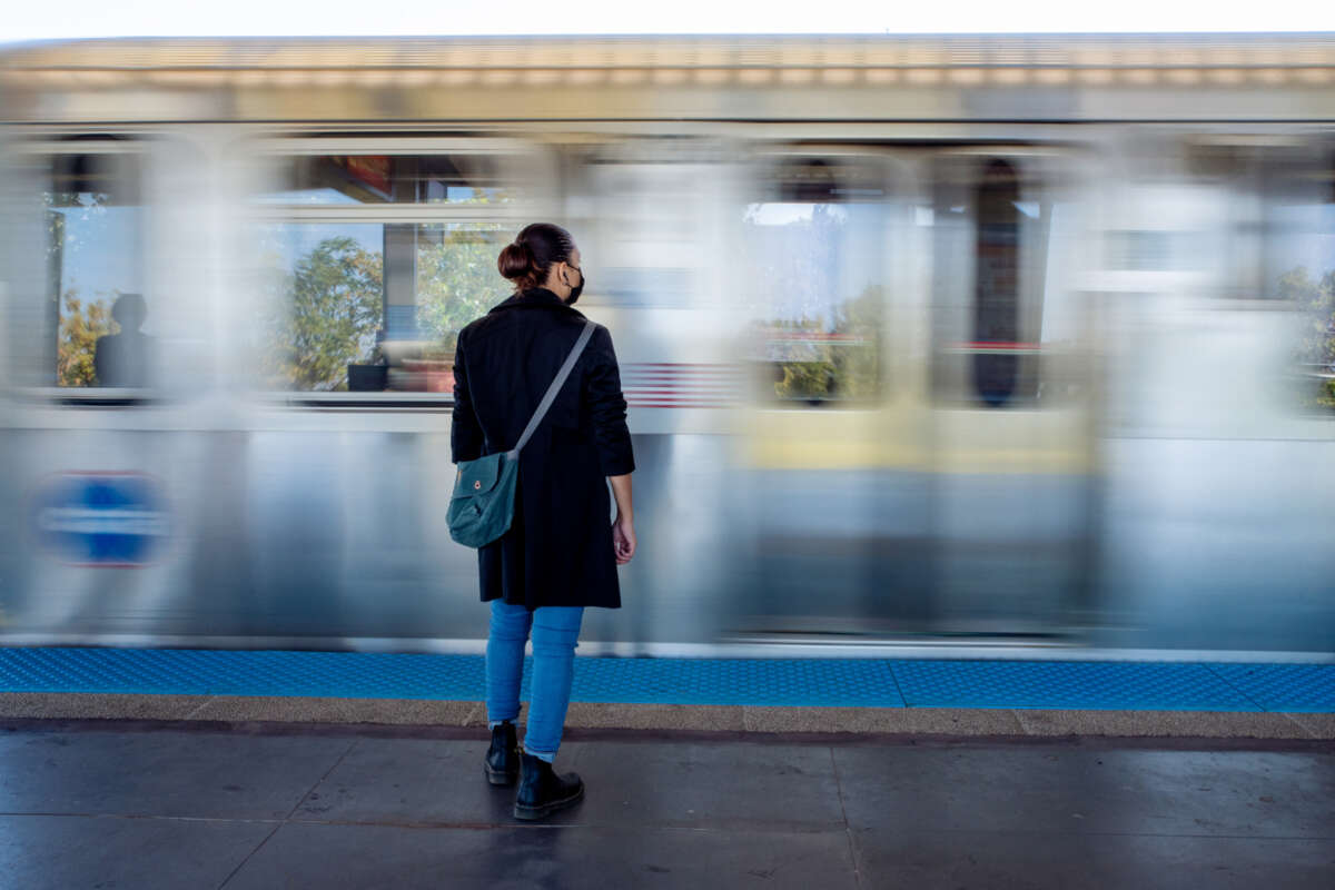 A woman stands on a train platform as the train goes by with a motion blur effect.