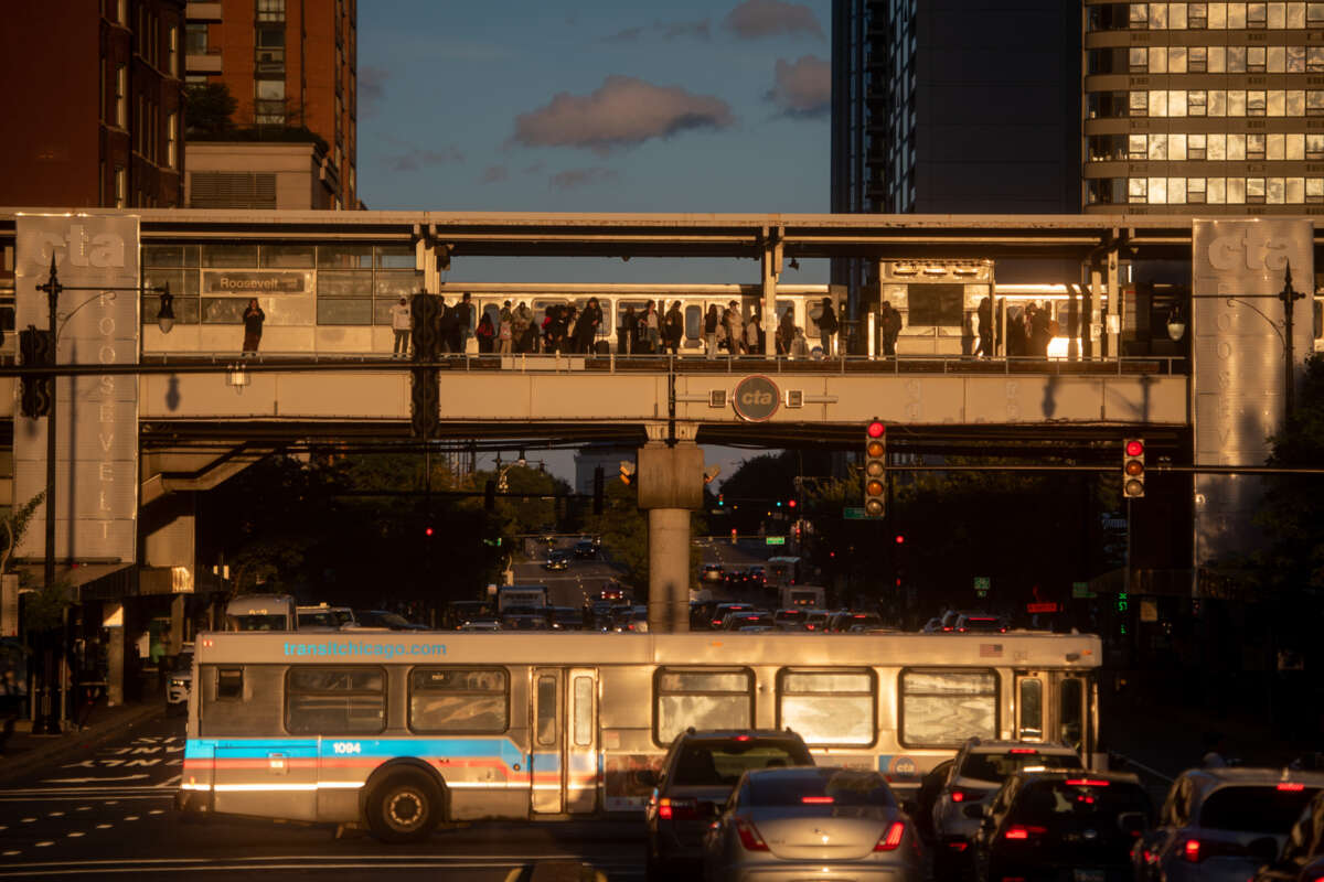 Dozens of people getting on and off an elevated CTA train with a CTA bus driving parallel to it on the street below.