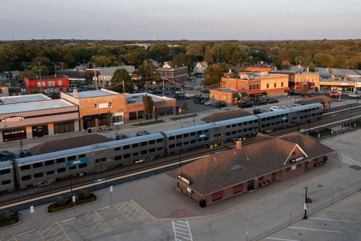A Metra train at a suburban station with a small, gently dense downtown.