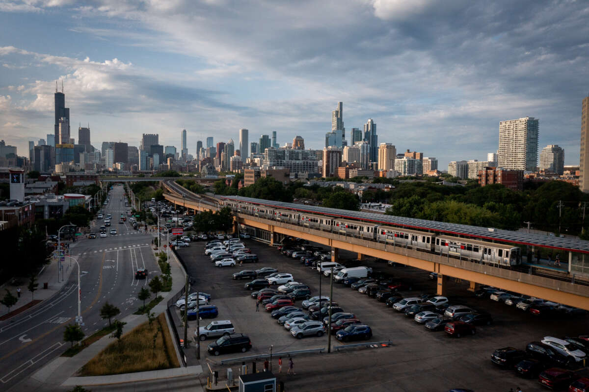 An elevated CTA train station with a full parking lot, and the Chicago skyline in the background.