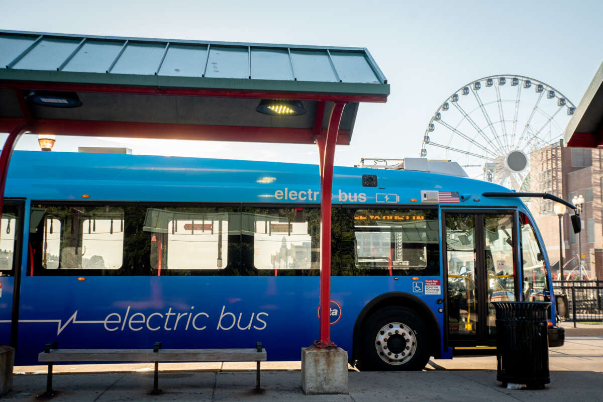 An electric CTA bus at a Navy Pier bus stop with a Ferris wheel in the background