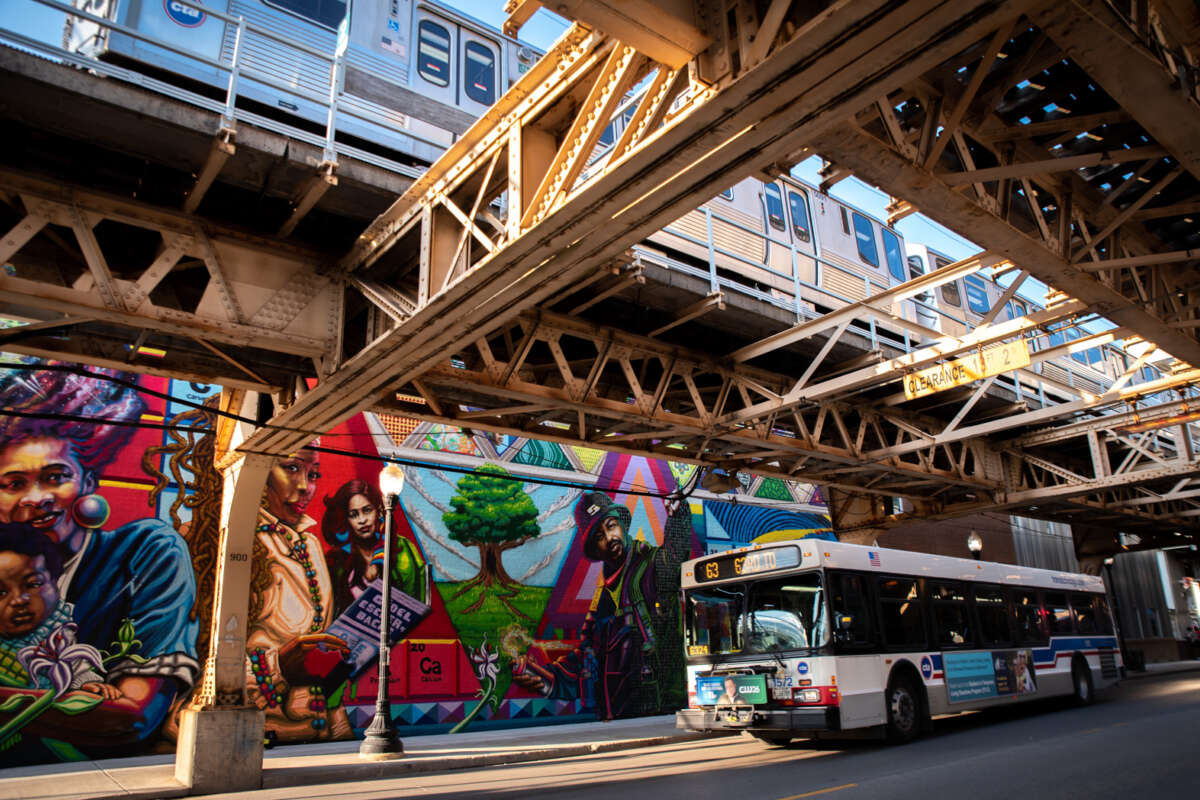 City of Chicago graffiti mural on building with CTA bus passing and CTA L train passing on tracks above.