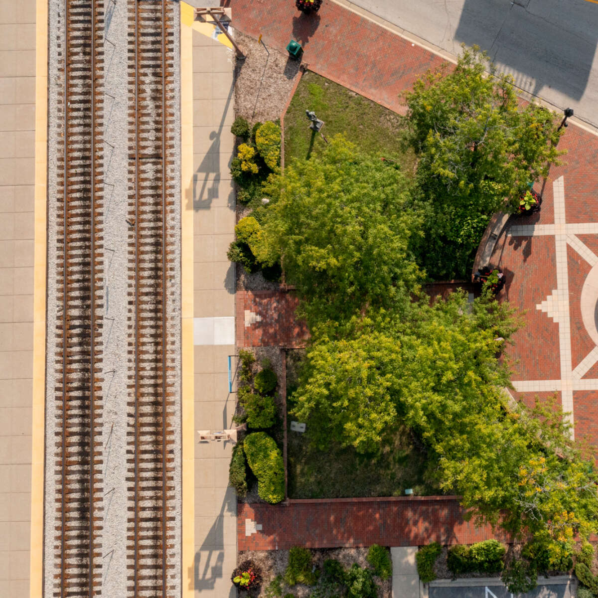 An aerial shot of train tracks, grass and trees, and a plaza with a fountain.