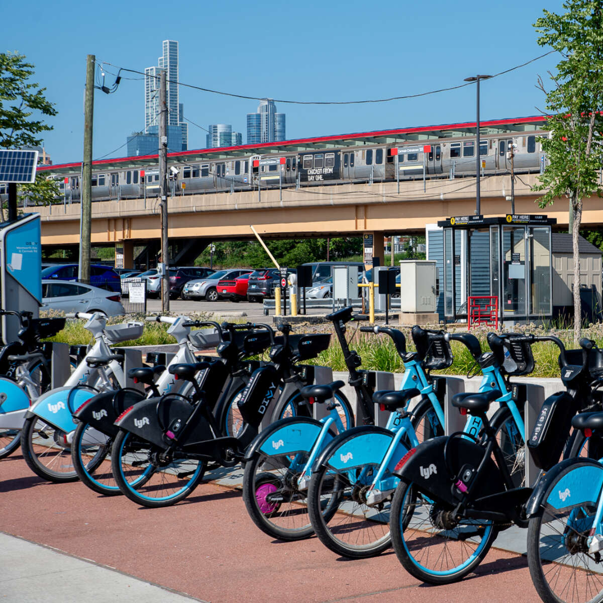 A Divvy bikeshare rack full of bikes with a CTA train at the Cermak Chinatown station and skyscrapers in the background
