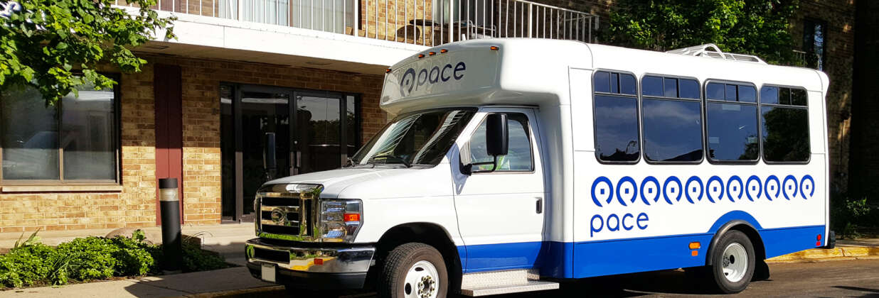 A Pace Paratransit vehicle parked outside of a multiunit residential building.