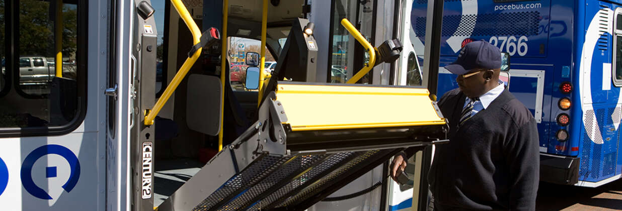 A Pace Paratransit vehicle driver operates the lift on the side of the vehicle, with a Pace fixed-route bus in the background.